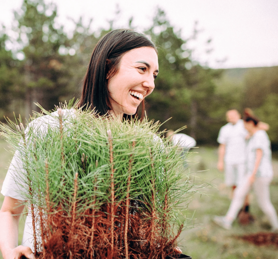 Woman smiling while holding seedling trees.