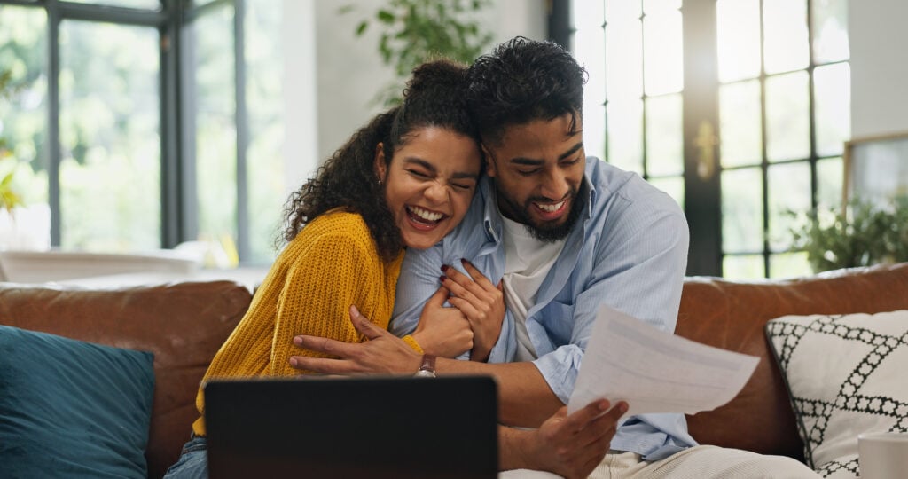 Happy, hug and couple with paperwork, financial planning or excited for home loan on website or app. Laughing, man and woman with document for mortgage, laptop and celebration with embrace in house.