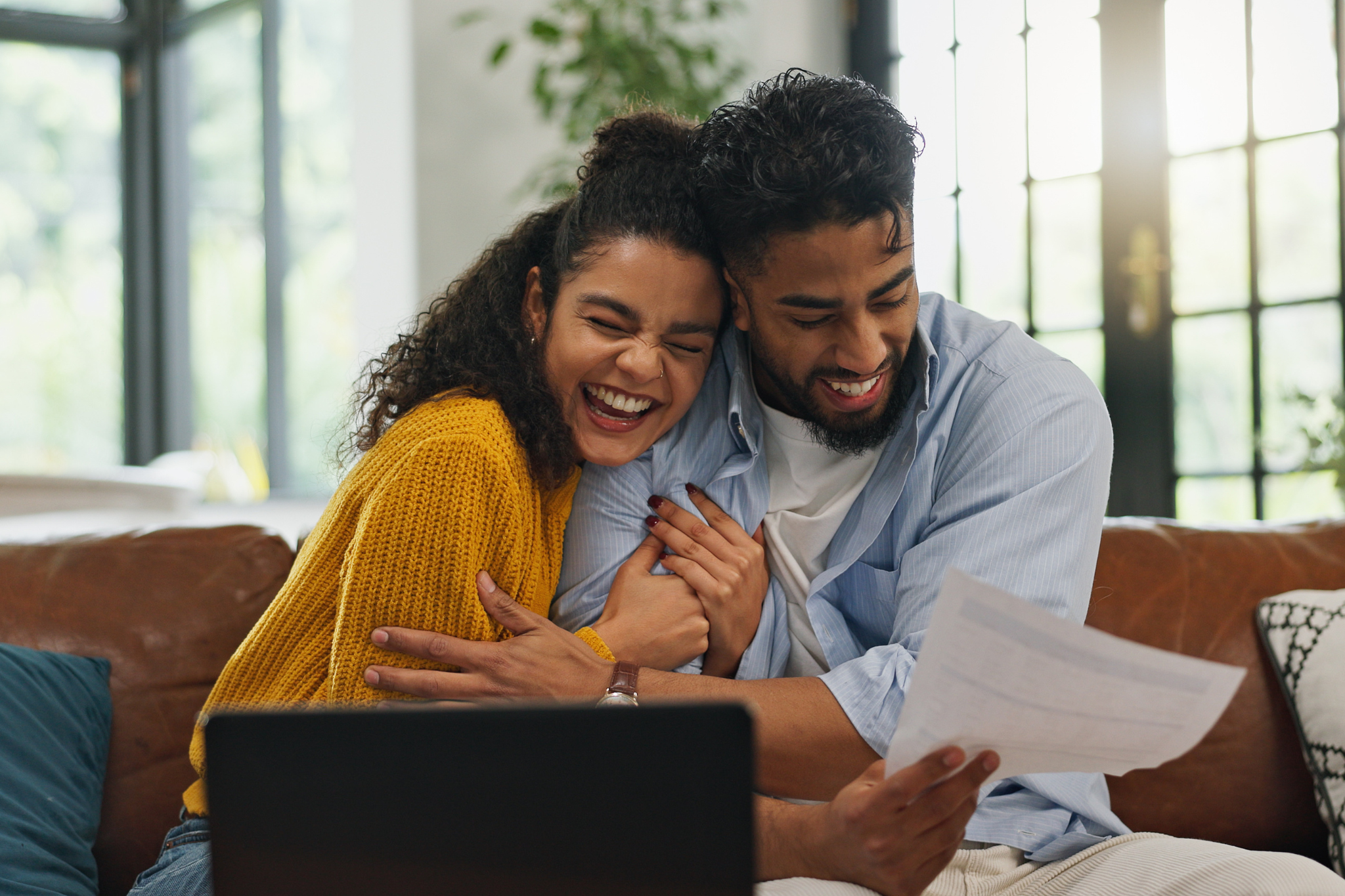 Happy, hug and couple with paperwork, financial planning or excited for home loan on website or app. Laughing, man and woman with document for mortgage, laptop and celebration with embrace in house.